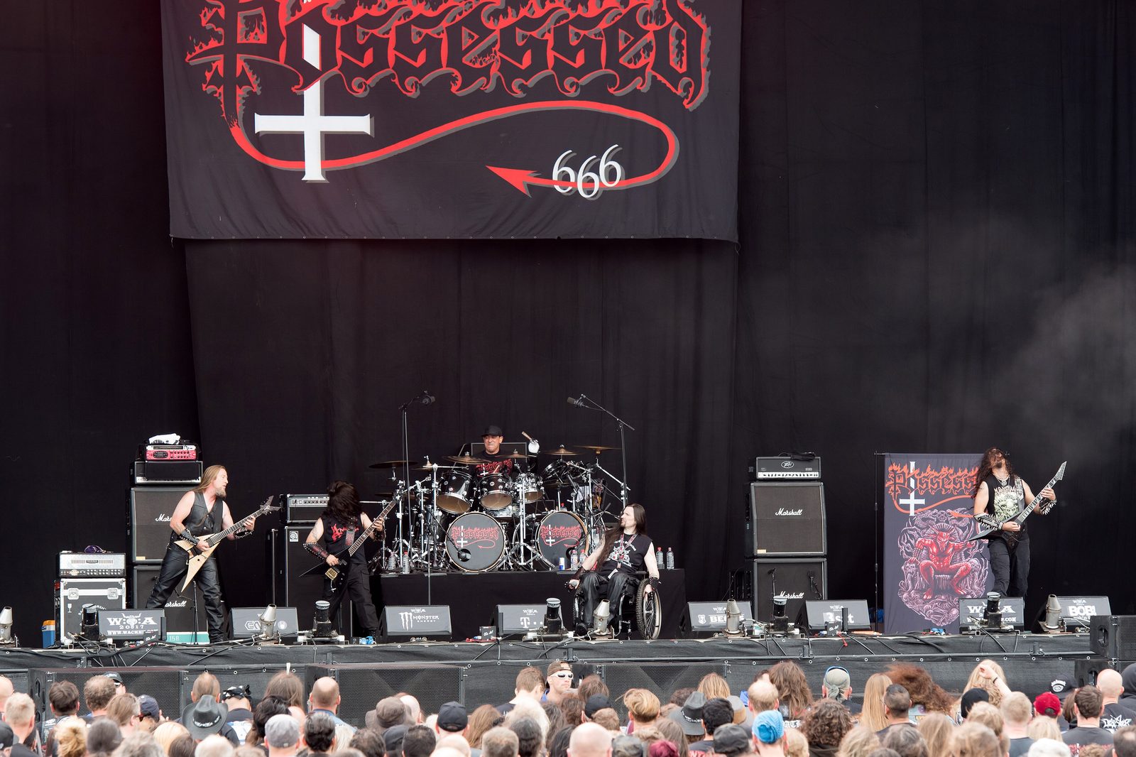 Possessed on a large open-air stage in daylight, a Possessed banner hanging above the band and a crowd packed in front of the barrier