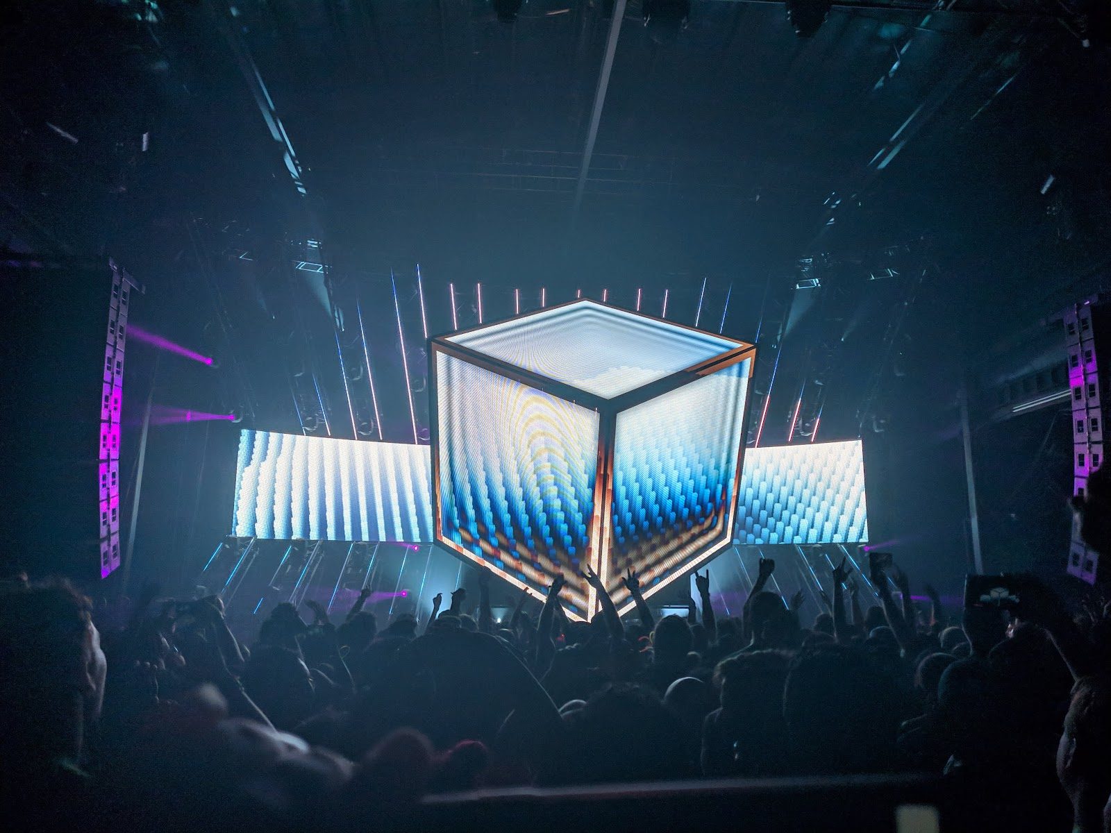 A crowd with raised hands facing a large lit stage at South Side Ballroom, a glowing video cube hanging over the stage