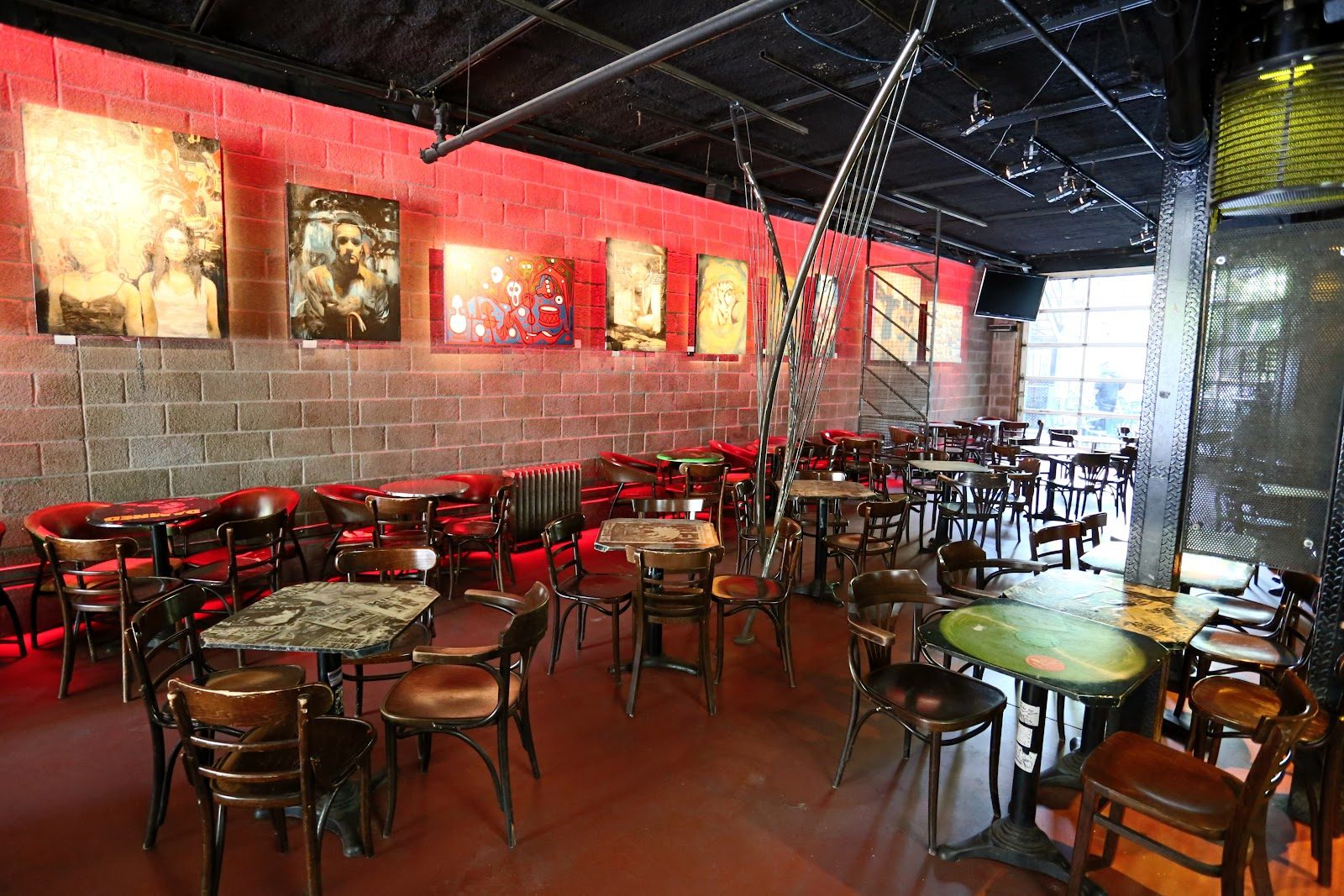 Inside Foufounes Électriques: wooden bistro chairs and graffiti-topped tables under red-lit cinder-block walls hung with paintings, a roll-up glass door at the back
