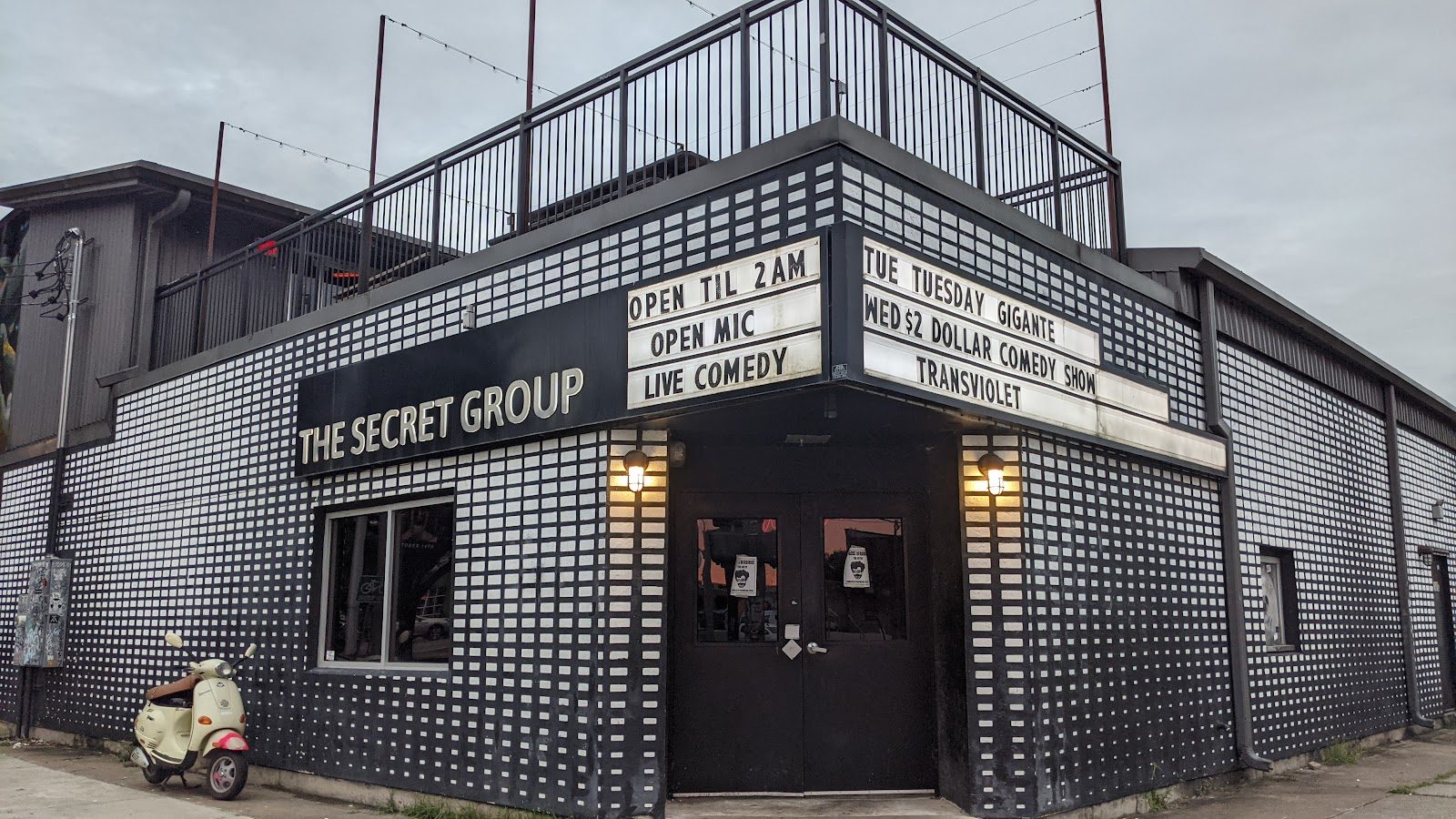 The corner entrance of The Secret Group in Houston, a black-and-white brick-pattern building with a lit marquee and a railed rooftop deck