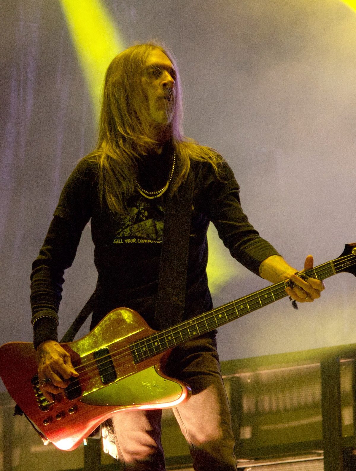 Rex Brown, long-haired, playing a red Gibson Thunderbird-style bass under yellow stage lights in 2023