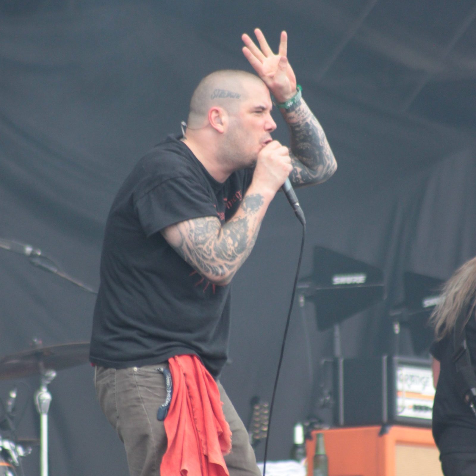 Phil Anselmo singing into a microphone with one hand raised, in a black T-shirt with a red cloth hanging from his belt, on an outdoor festival stage